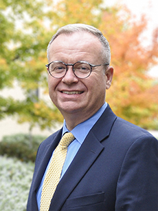 Older man with glasses, in suit, smiling.